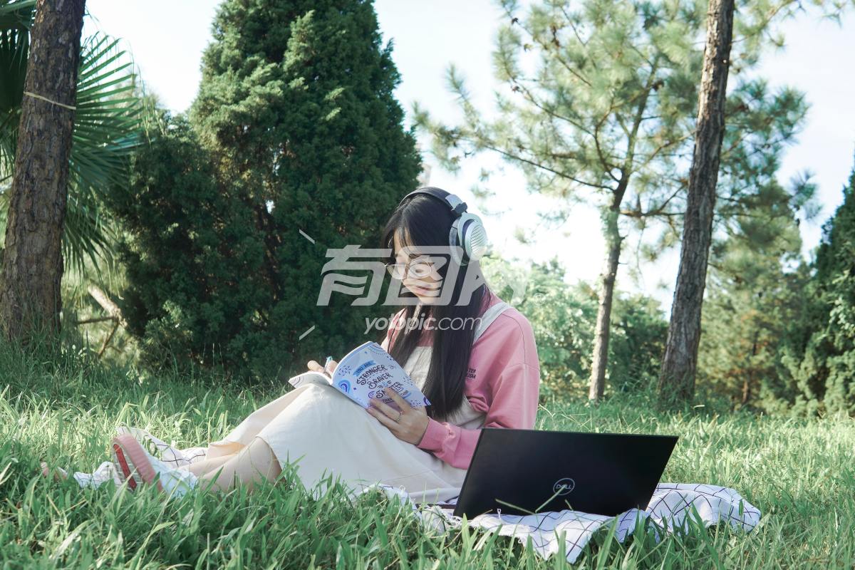 戴着耳机的女孩在草坪中看书