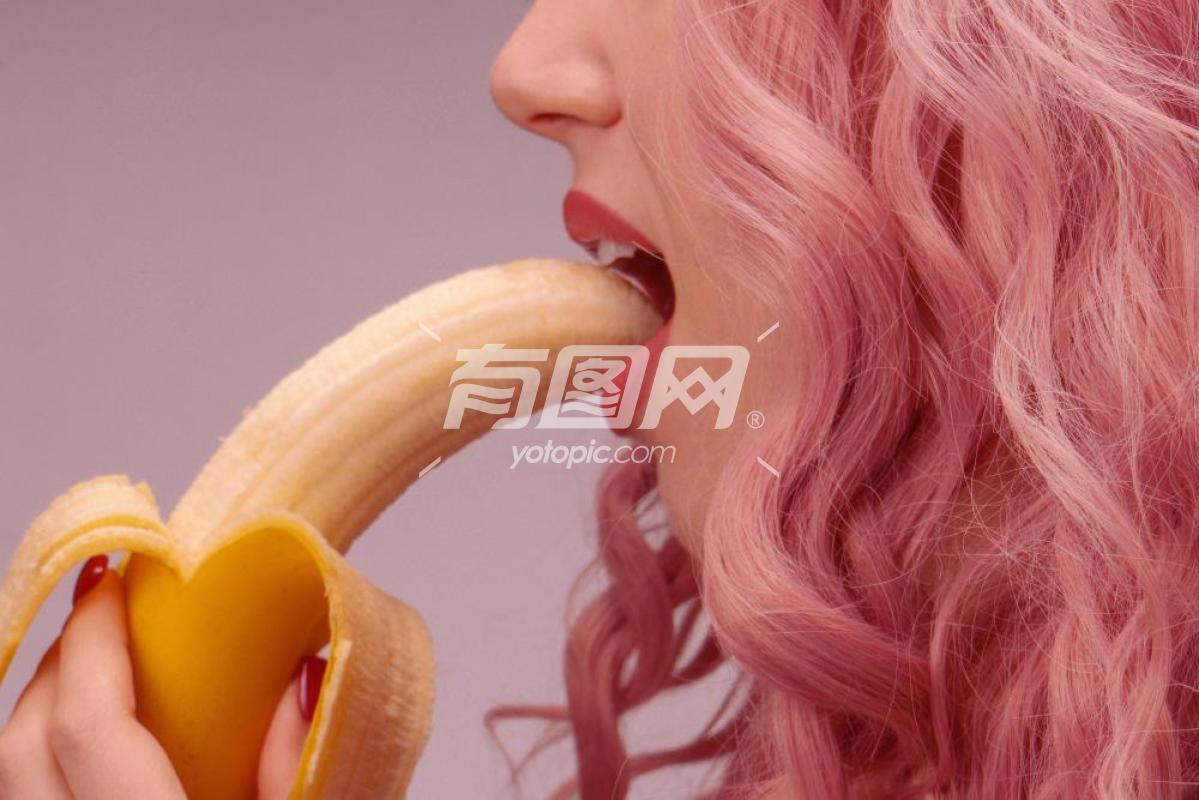 粉红色卷发的女人正在吃香蕉特写